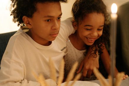 Two children enjoying a cozy dinner at home by candlelight with a warm family atmosphere.
