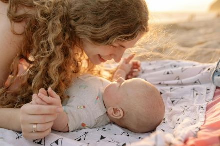 A joyful moment between a mother and baby on a sunny beach, embracing affection and love.
