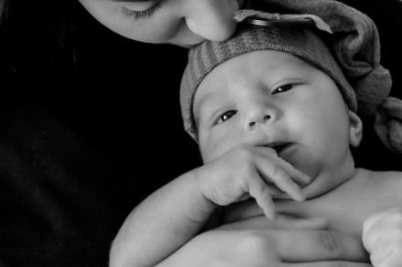 Intimate black and white portrait of a mother gently holding her newborn baby.