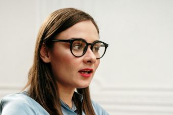 A professional woman in glasses engaging in a thoughtful indoor discussion.