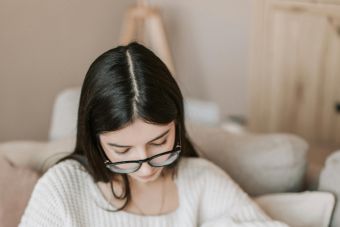 A young woman writes in a notebook while sitting comfortably on the sofa at home.