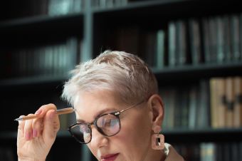 Elderly woman reading a document, seated in a library setting. Thoughtful and intellectual ambiance.