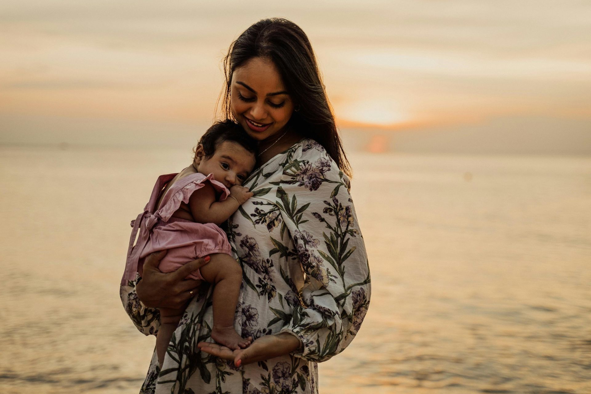 A serene moment of a mother holding her baby during sunset at the beach.